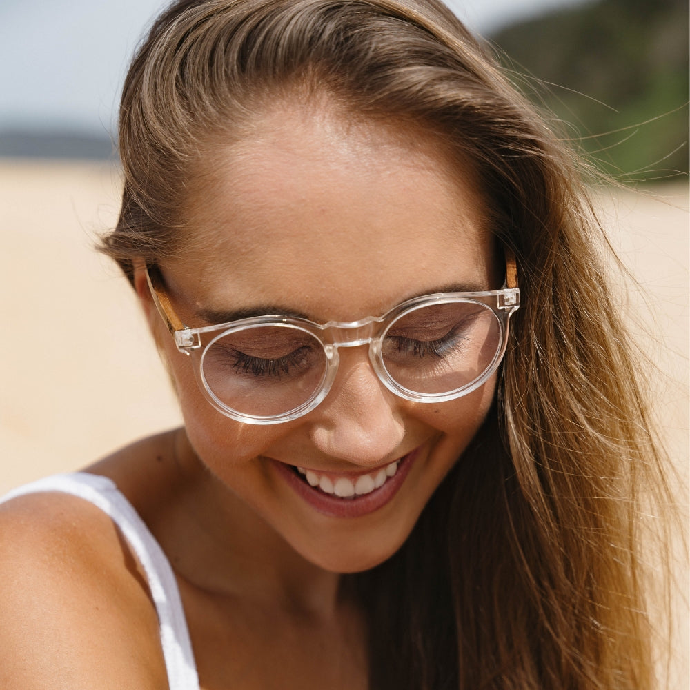 Woman wearing SOEK Wineglass Bay blue light magnifying reading glasses outdoors, smiling, close-up image.