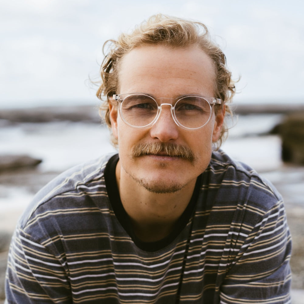 SOEK Wineglass Bay blue light magnifying reader glasses worn by man outdoors with ocean background.