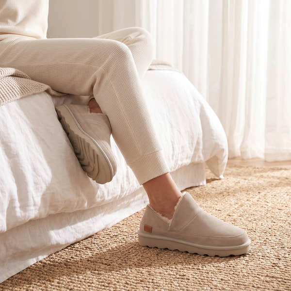 Strive Alaska grey suede slippers, worn while sitting on a bed