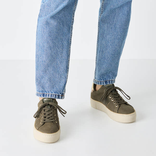 Tamaris Ladies Olive Nubuck Leather Lace-Up Trainers with white rubber soles and gold eyelets, paired with blue jeans.