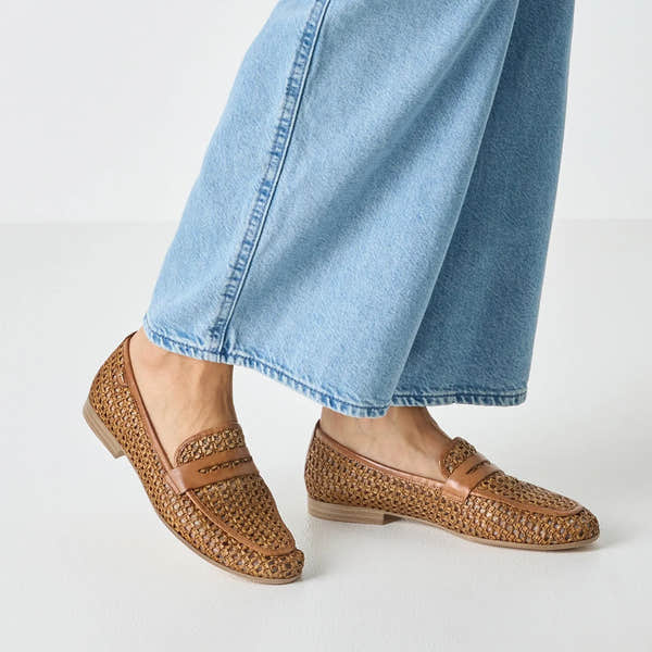 Tamaris loafers in cognac leather and textile, woven design, slip-on style with small heel, worn with light blue jeans.
