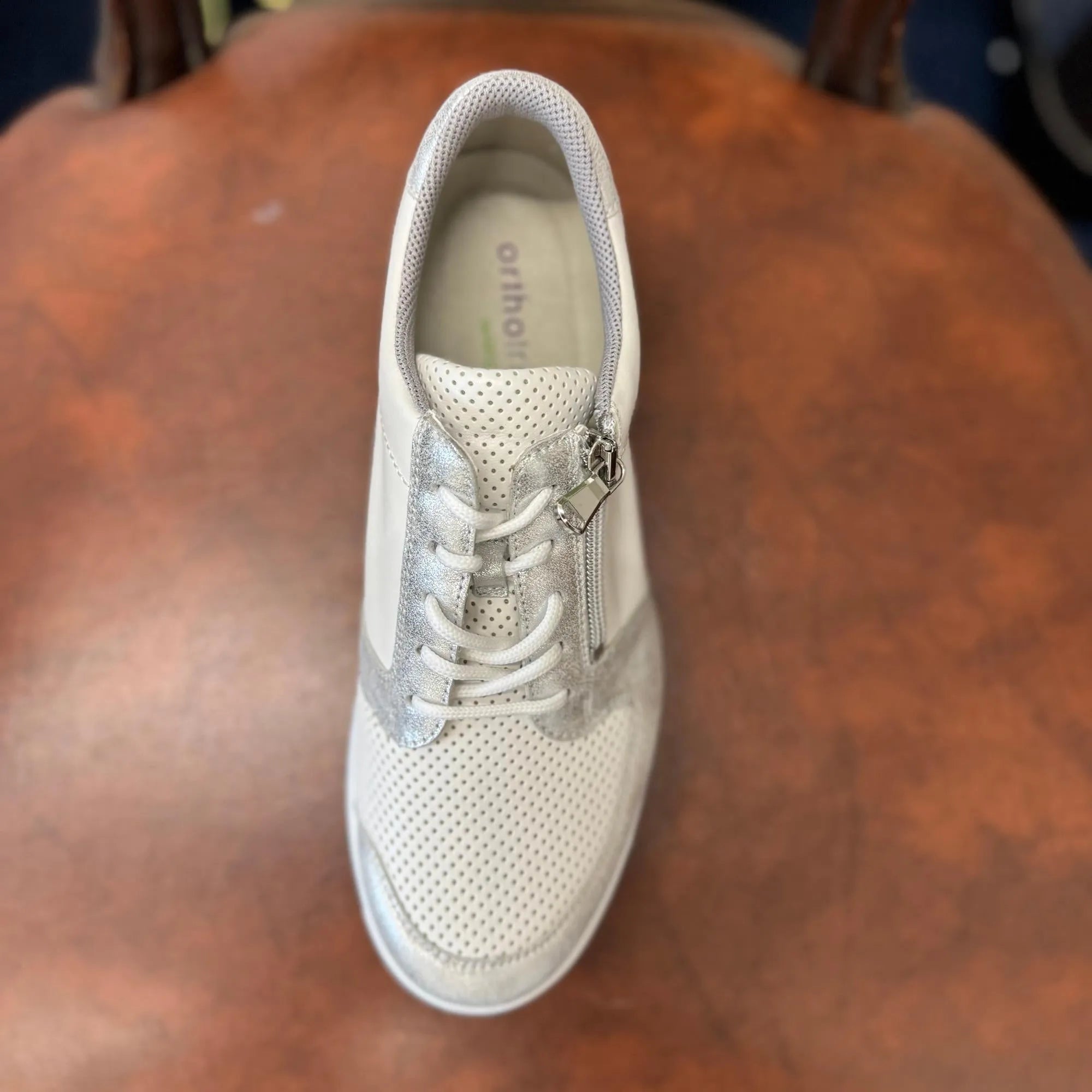 Waldlaufer K-Funky women's wide fit sneakers with silver and white leather, zip and lace closure, arch support, on wooden surface.