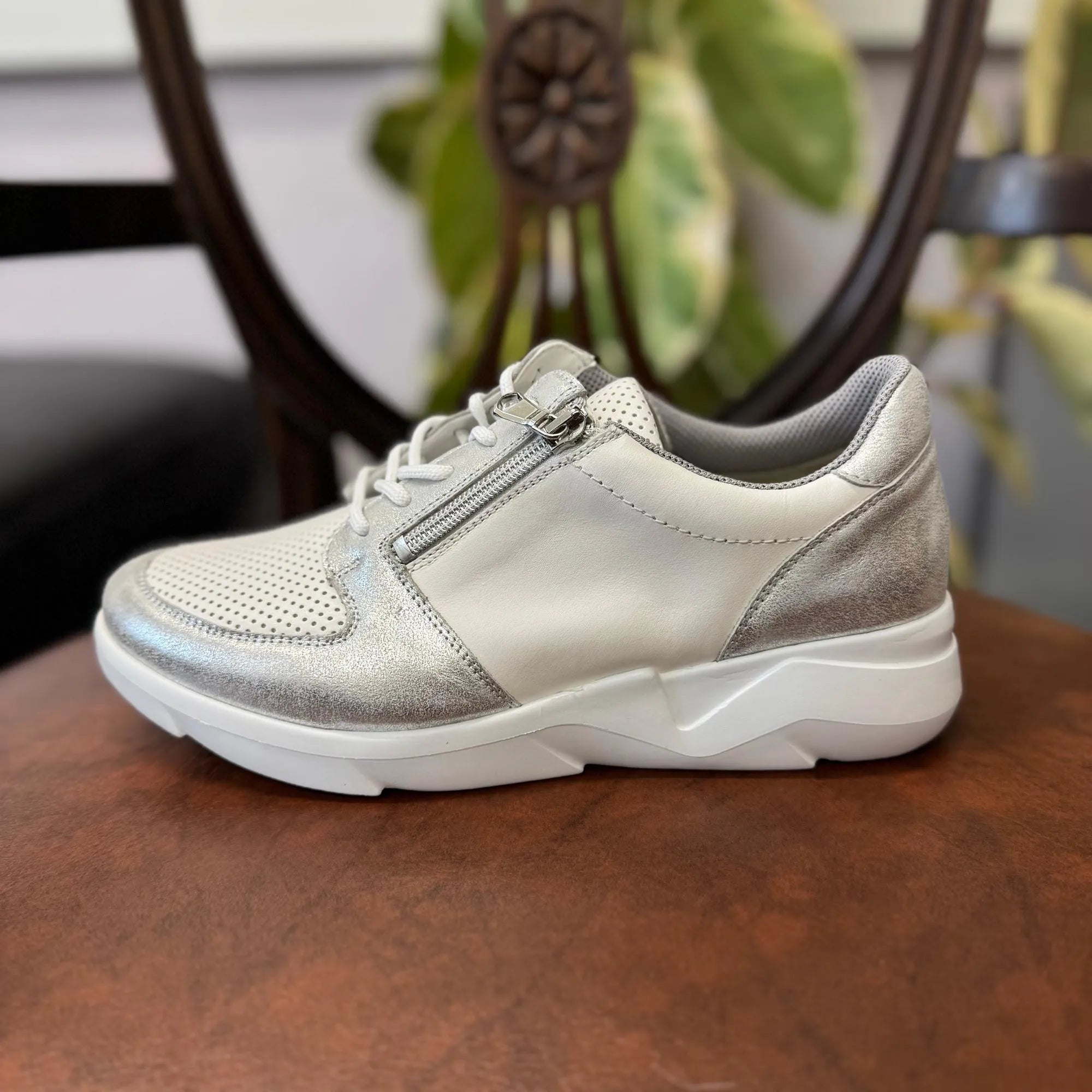 Waldlaufer women’s wide-fit silver and white leather trainer with arch support, zip and lace fastening, on brown surface.