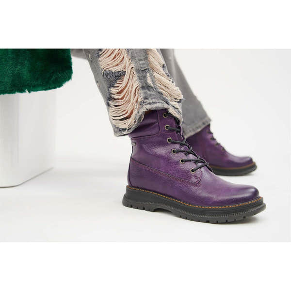 Women's purple waterproof vegan ankle boots with lace-up front, stylish distressed denim jeans, and green faux fur coat.