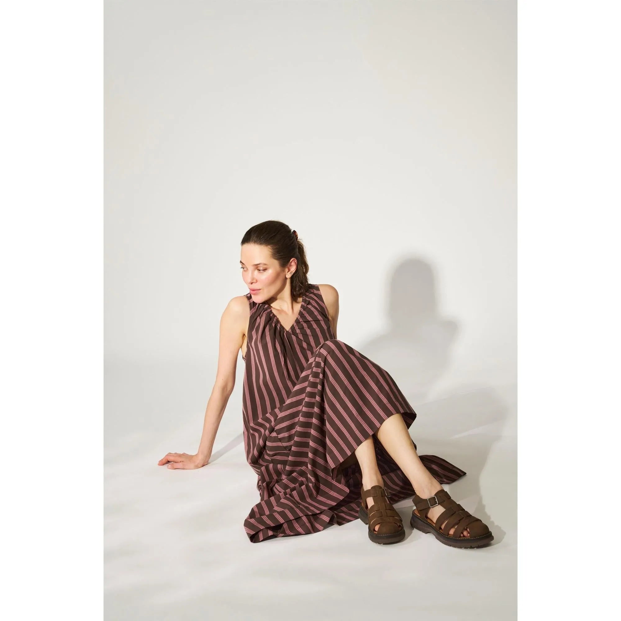 Women's brown touch fastening sandals with wide straps, paired with a long striped dress, on a white background.