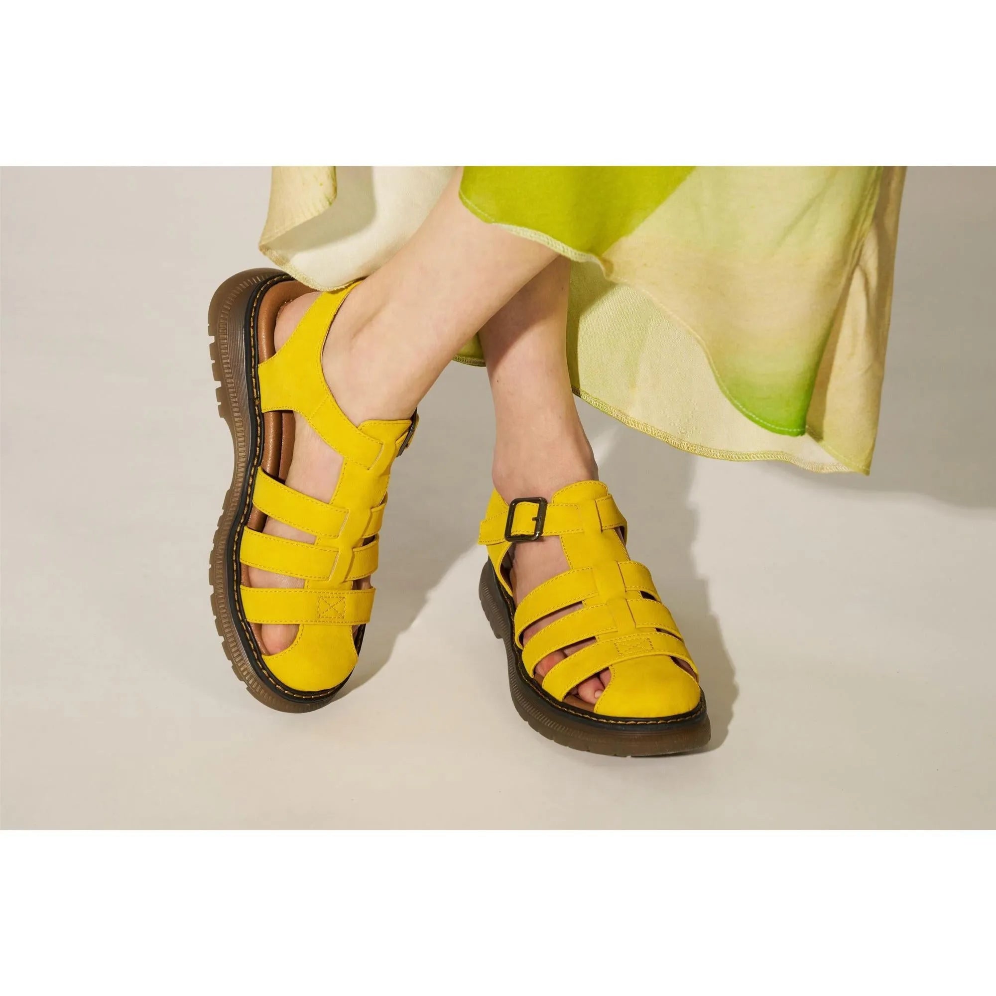 Yellow touch-fastening sandals with open toes, multiple straps, and thick black soles, worn with a green and beige dress.