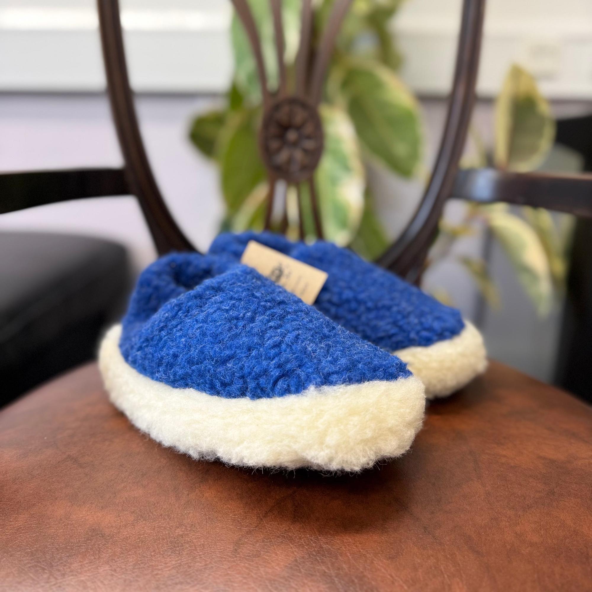Yoko unisex deep blue wool slippers with cream fleece lining, cozy and comfortable indoor footwear on wooden chair.