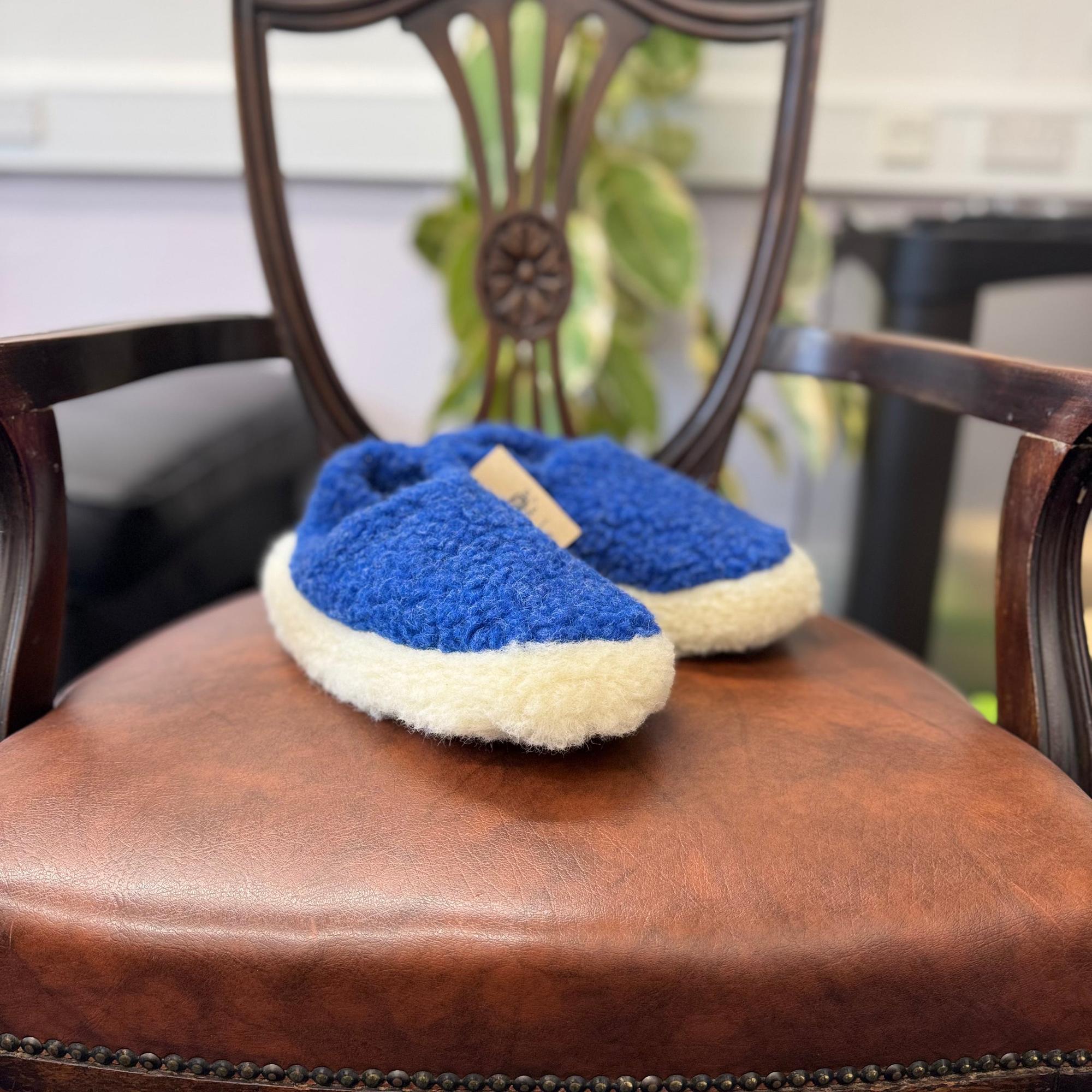 Yoko unisex deep blue wool slippers on a wooden chair with leather seat, cozy and comfortable footwear for everyday wear.