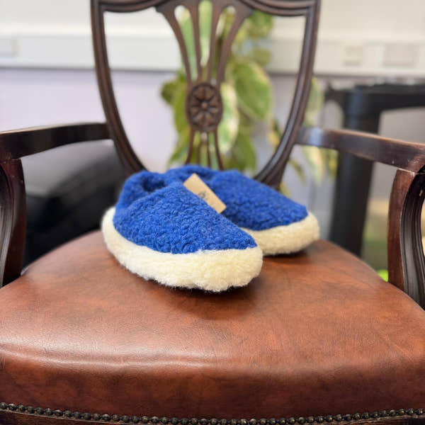 Yoko unisex deep blue wool slippers on a wooden chair with leather seat, cozy and comfortable footwear for everyday wear.