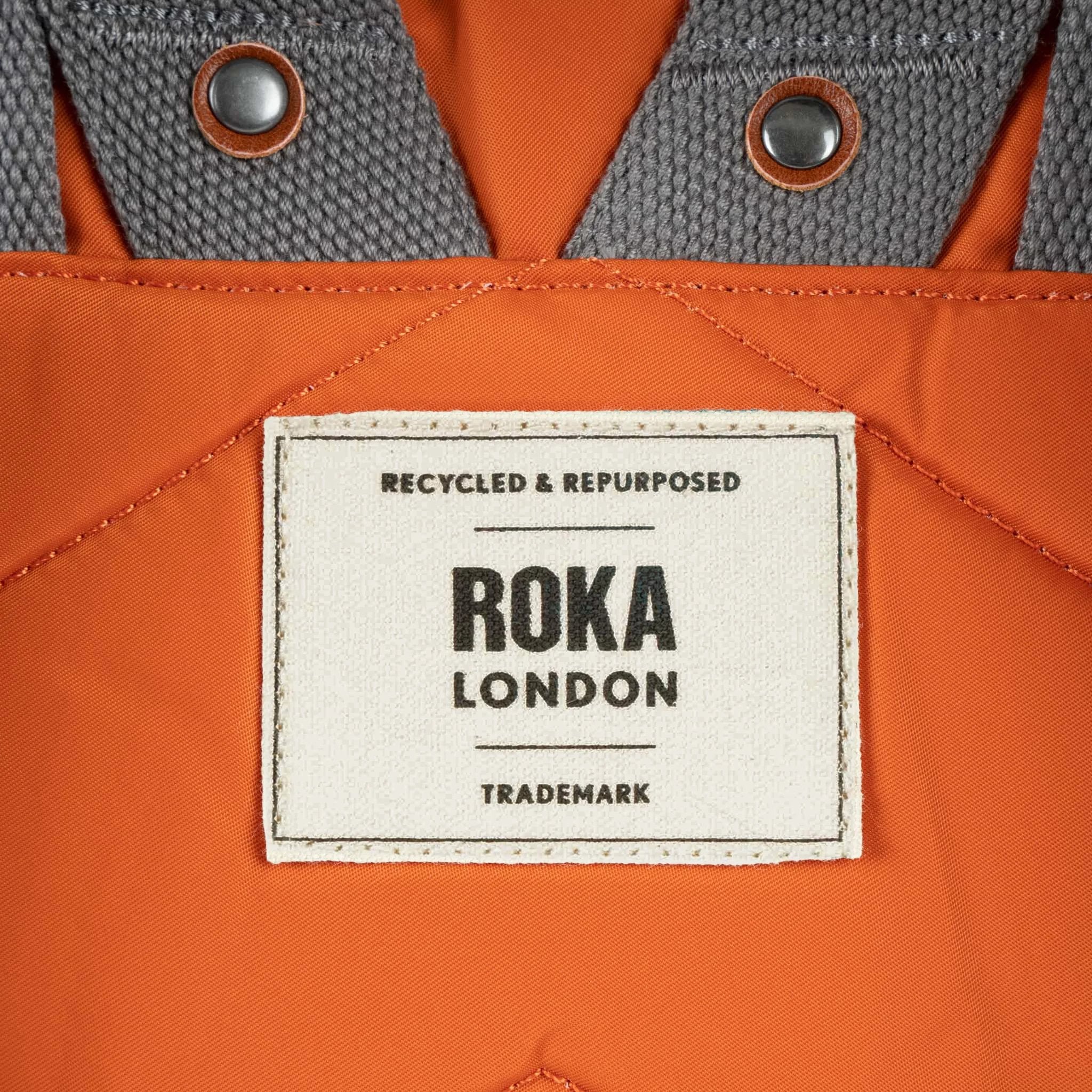 Roka Canfield Medium Burnt Orange Recycled Nylon Backpack, brand label detail.