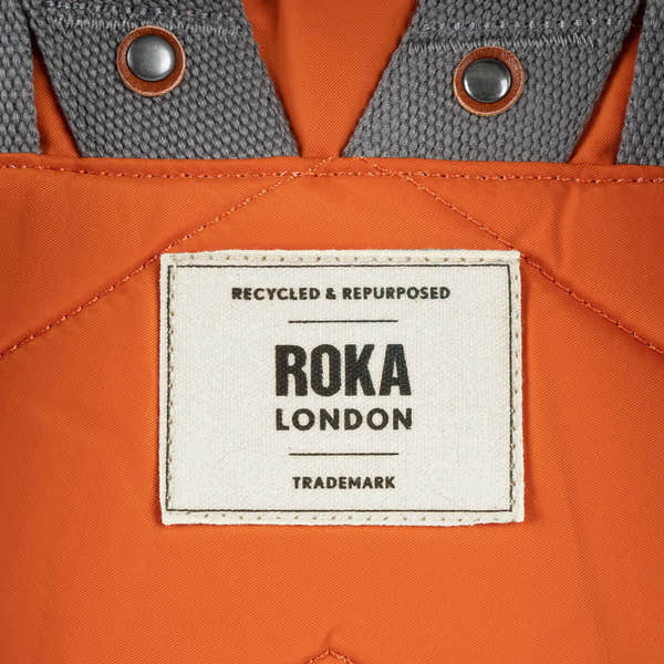 Roka Canfield Medium Burnt Orange Recycled Nylon Backpack, brand label detail.