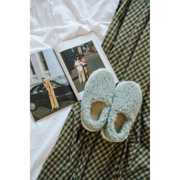 Yoko Full unisex Green wool slippers styled on a bed with a magazine, overhead lifestyle view.