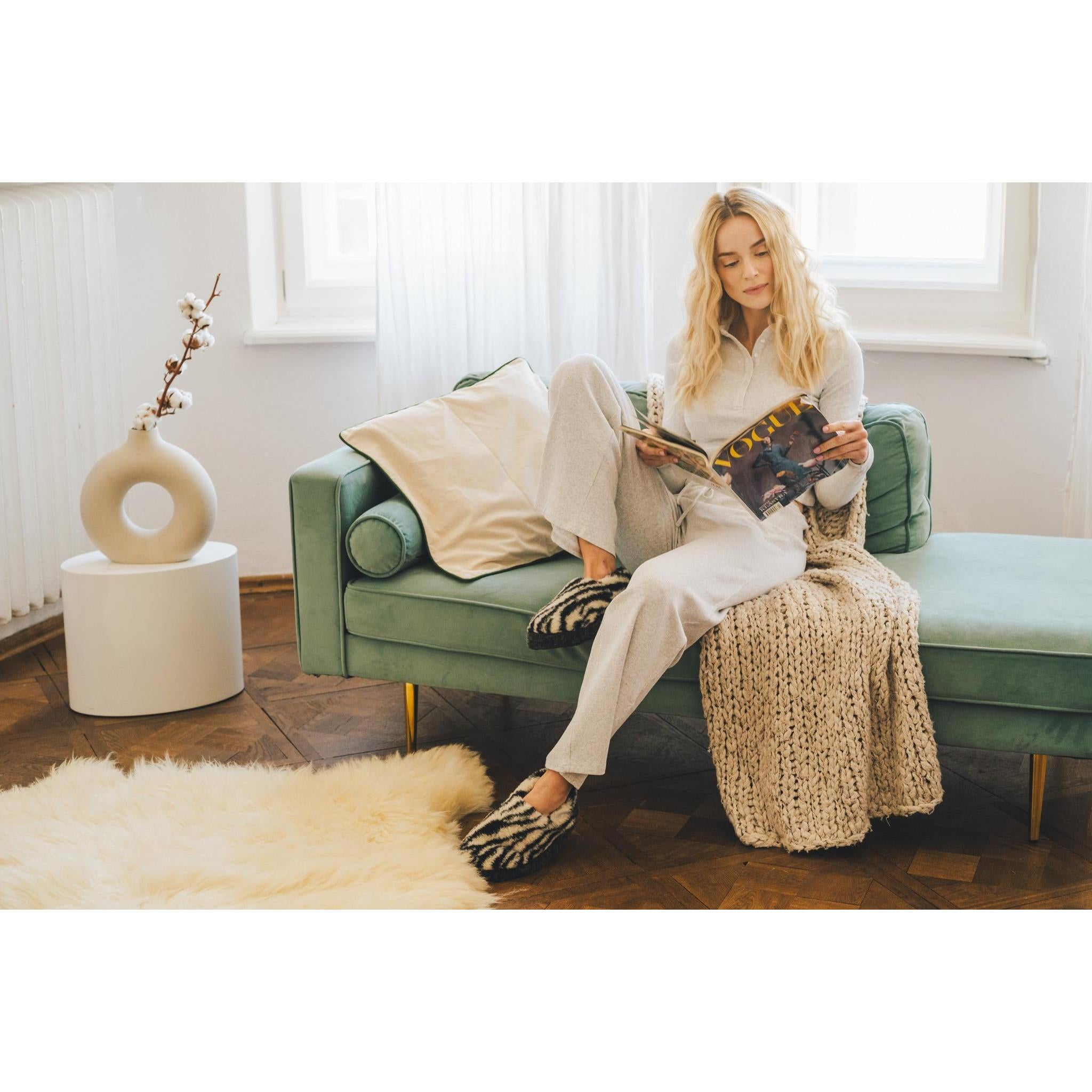 Yoko Full unisex Zebra Print wool slippers worn while reading on a sofa, lifestyle view.
